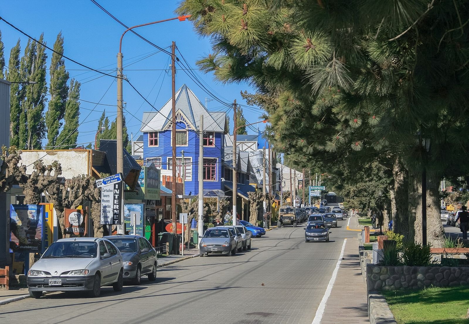 Rua arborizada no centro de El Calafate, com lojas e restaurantes